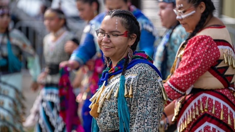 A person wearing traditional Indigenous regalia is seen smiling.