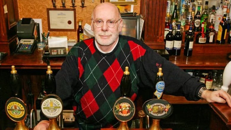 A man wearing a black and red sweater is shown in front of four beer taps.