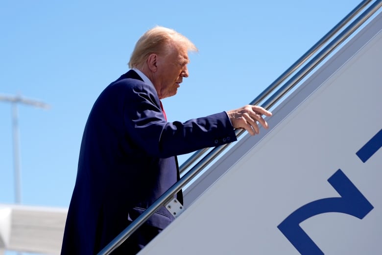 A person hold the railing as they walk up stairs leading to an airplane.