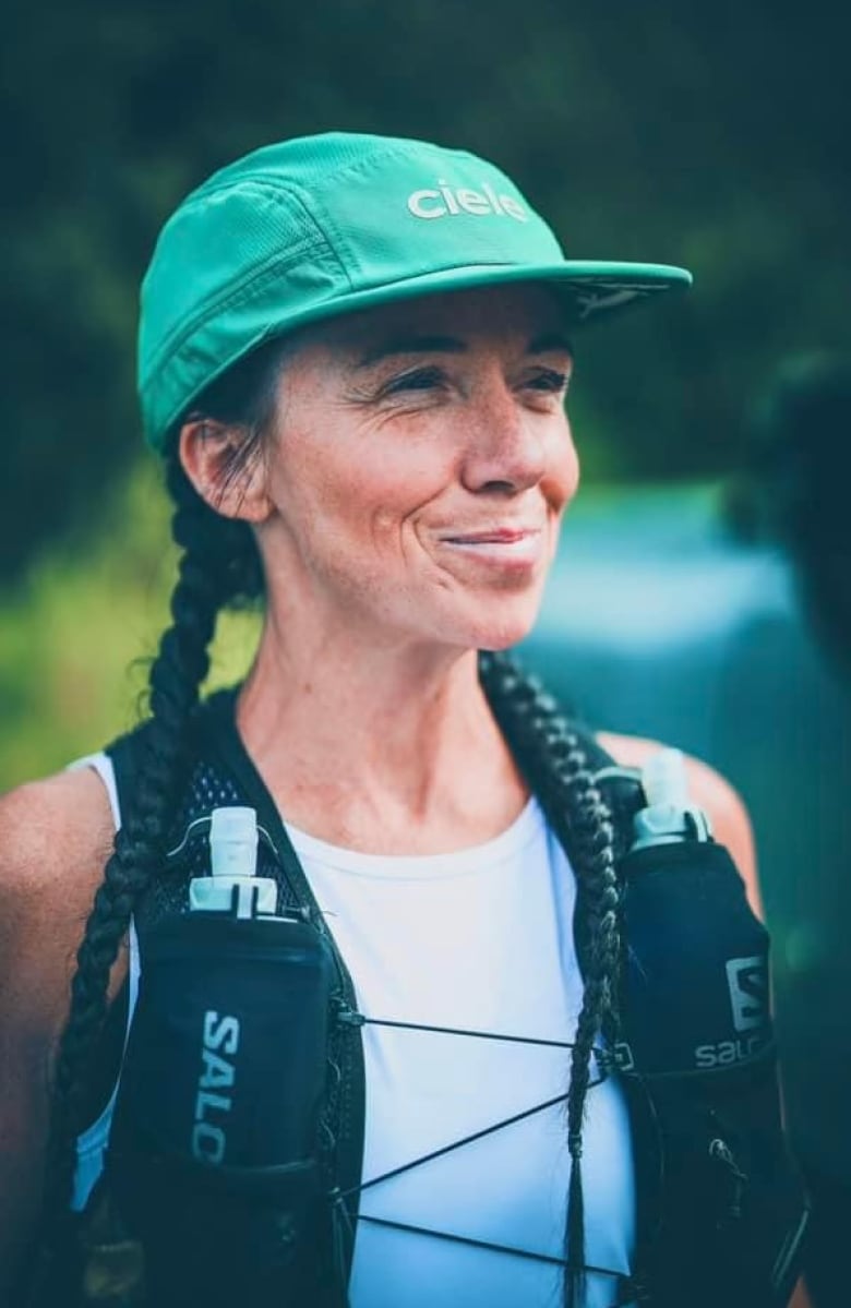 A woman in a white shirt and green baseball cap smiles at something just off camera.