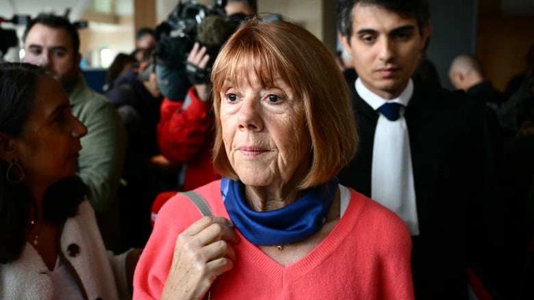 An older woman in a red sweater stands in a crowd