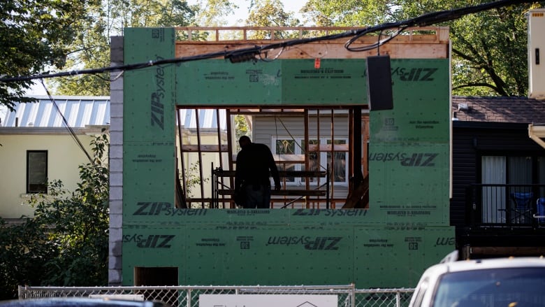 A person's silhouette is visible from inside a partially constructed home.