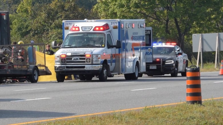 A Halton paramedic ambulance sits on the side of the road with an Ontario Provincial Police car behind it, both vehicles have their light bars on.