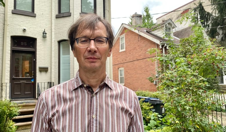 Serguei Zernov wears a striped collared shirt and stands in front of a house. 