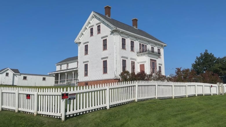 a white historical home with a white picket fence and green lawn