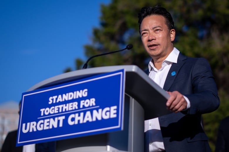 A man speaks at a podium marked 'Standing together for urgent change.'