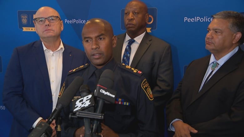 Police chiefs from Edmonton, Peel, Nashville and Albuquerque standing in front of a blue backdrop and speaking to the media at a police conference 