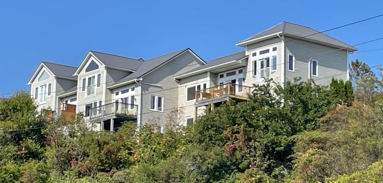 A series of conncted new houses sit on the edge of a bluff under a bright blue sky.