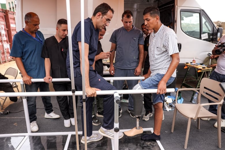 A prosthetics specialist helps a man walk with a new prosthetic leg.