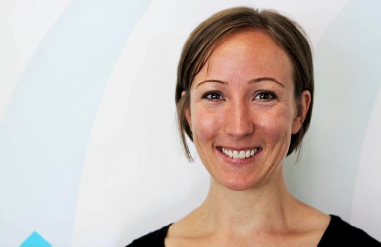 A smiling woman with brown hair pulled back, smiles into the camera.