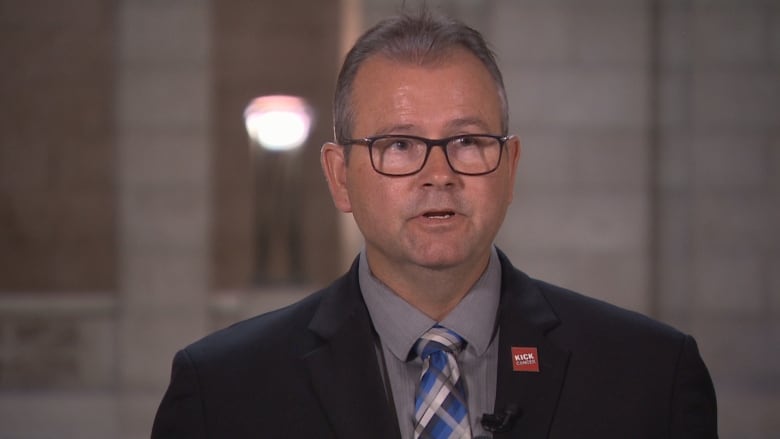 A man in glasses and a suit speaks.