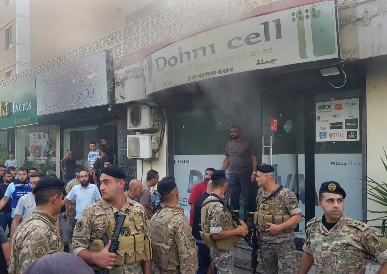 Six Lebanese soldiers in uniform gather outside a smoking, damaged mobile shop.