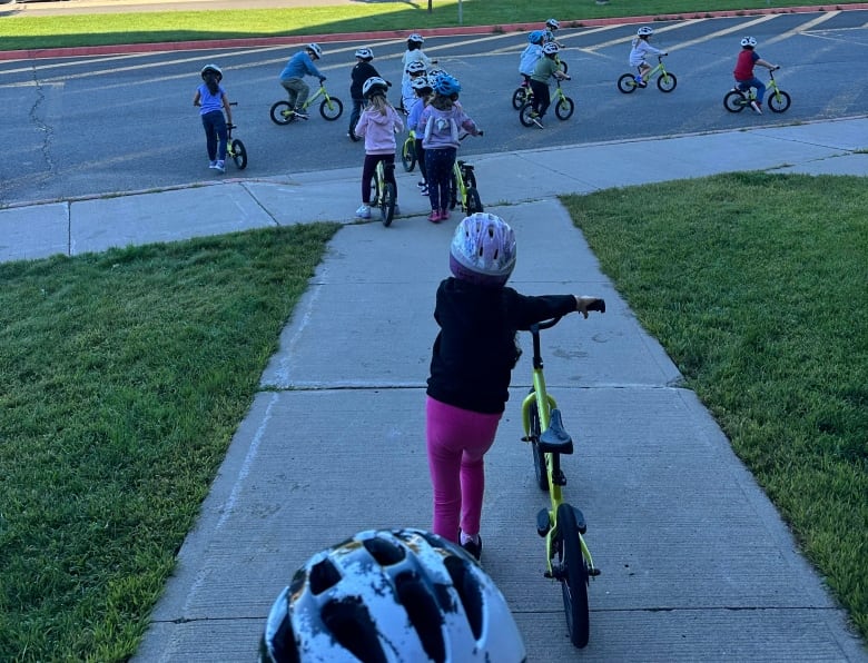 Elementary aged students riding balance bikes outside their school on a sunny day.