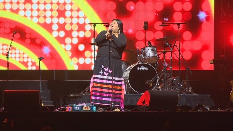 A woman holds a microphone while singing on stage at an event. 