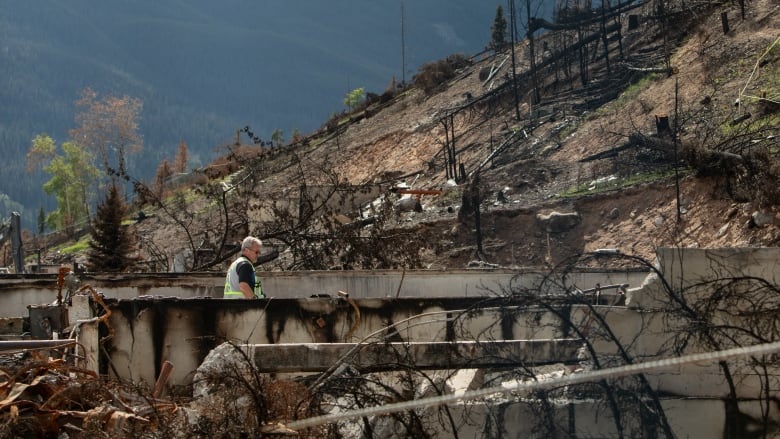 A man walks in a mountain of burned structures.