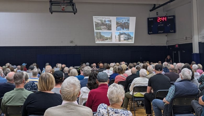 Dozens of people sitting and watching a presentation in what looks like a school gymnasium.