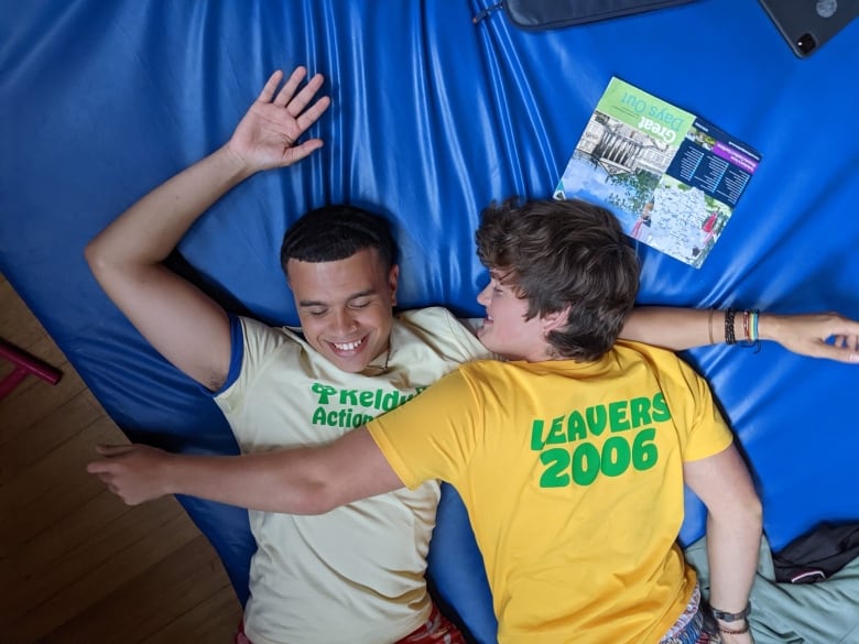 Two smiling young men lay on a bed. 