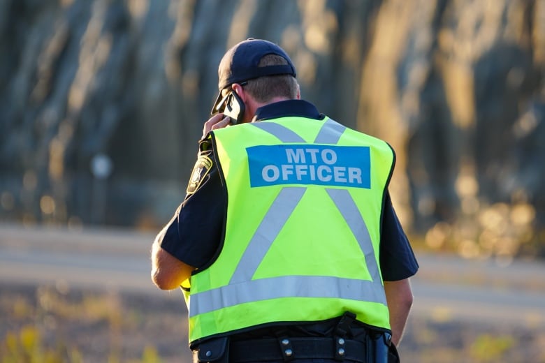 A person wearing a florescent vest is seen standing on a road, taking a phone call.