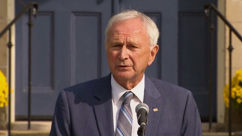 A man with grey hair, wearing a suit, speaking into a microphone