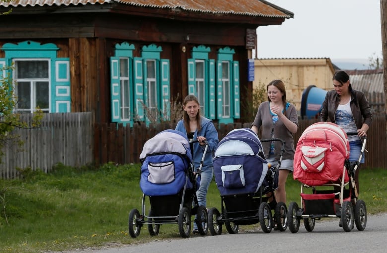 Three women push strollers on a street.