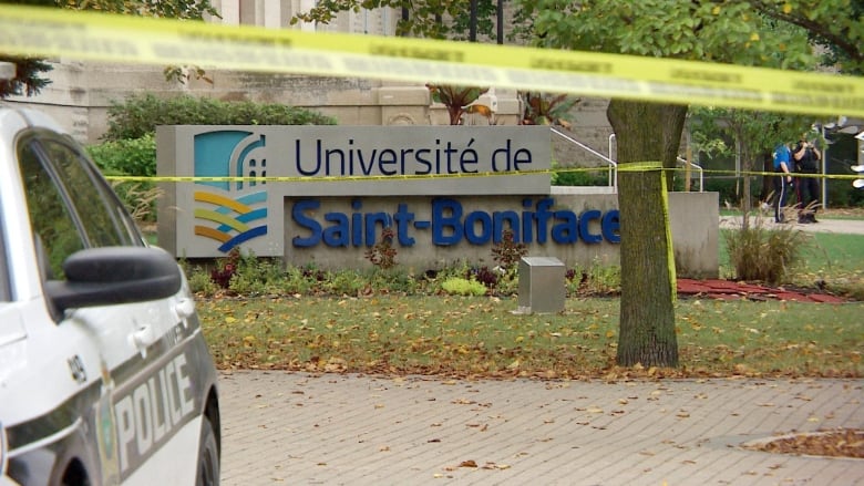 A school sign is pictured, with police tape and a police cruiser in front of it.