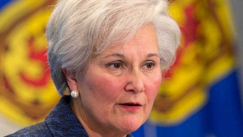 Woman with short gray hair and pearl earring in front of Nova Scotia flag.