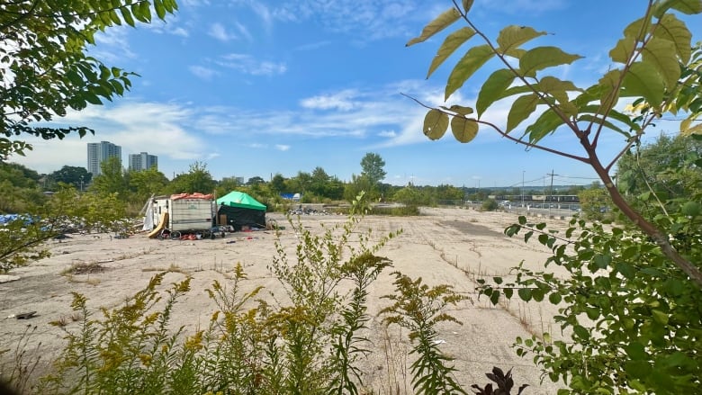 A plot of land surrounded by vegetation. A tent and an RV sit on the left side of it.