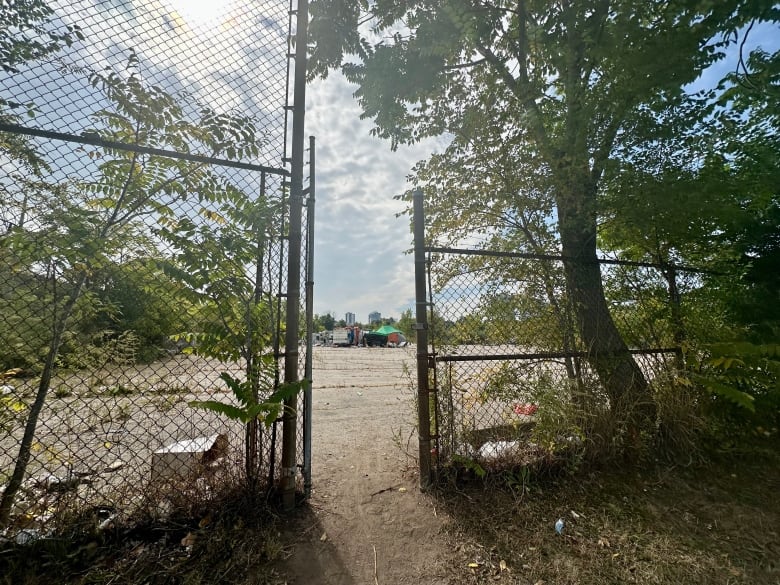 A metal gate open to a plot of land surrounded by vegetation with a tent and an RV sitting on the left area of it.