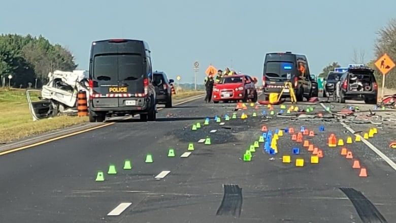 Police vehicles and coloured evidence markers on a closed highway after a crash.