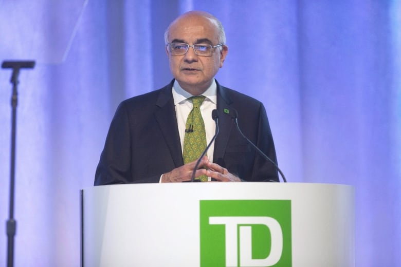 A man stands behind a podium. The podium has the TD bank symbol on it. 