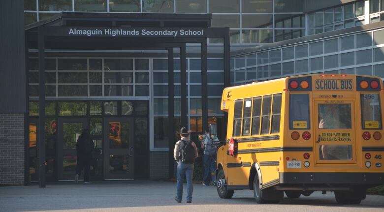 A student in a cowboy hat walks past a school bus into a high school 