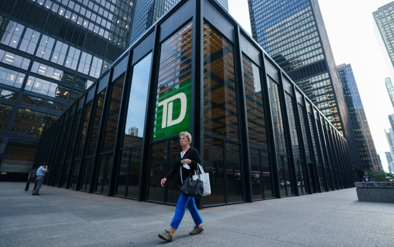 A person walks in front of the corner of a TD Bank. 