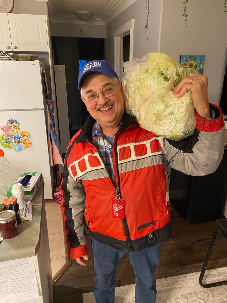 A man holds half a big cabbage over his shoulder. 