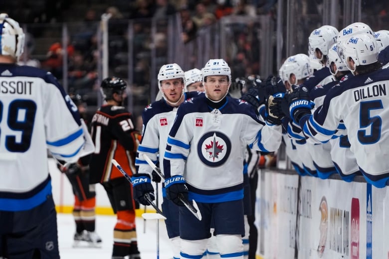 A man with a helmet and a hockey stick walks by a row of people.