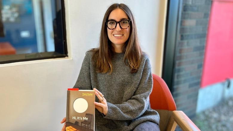 A smiling woman sitting in a chair and holding up a book.