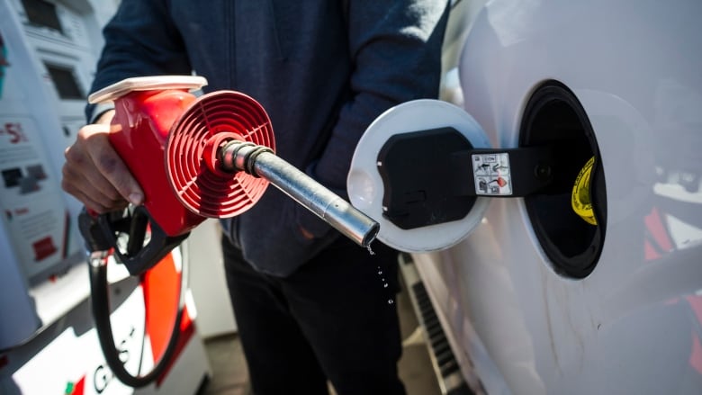 A close-up of a gas nozzle being brought to the open port at the side of a car. 