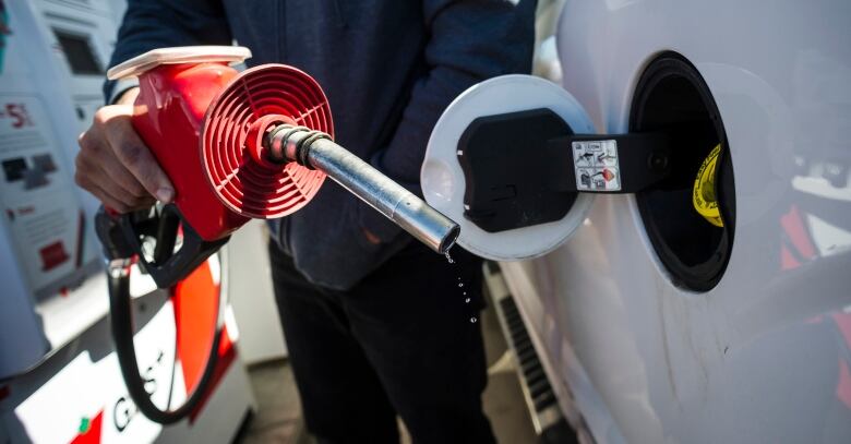 A close-up of a gas nozzle being brought to the open port at the side of a car. 