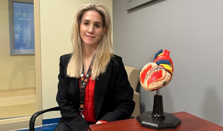 Photo of Dr. Mali Worme seated beside a model of a human heart. 