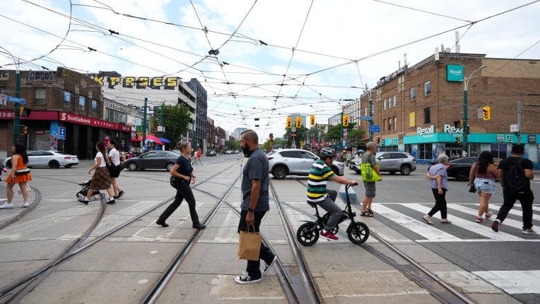 People cross the road at an intersection with streetcar wires visible overhead. 