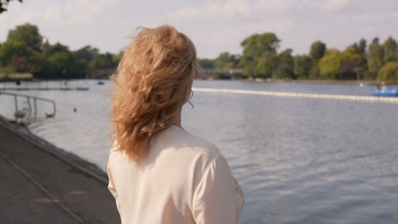 A woman with her back to the camera looks out across a river.