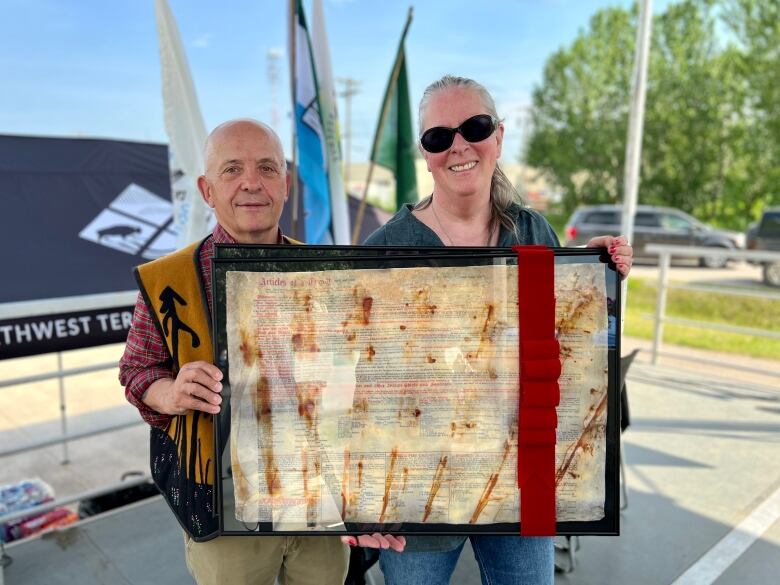 A man and woman stand outside, holding up a framed document.