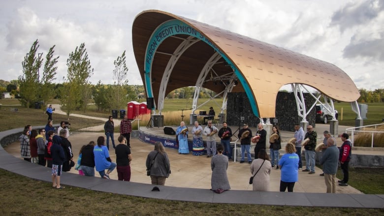 A drum group and prayer circle stands by a stage.