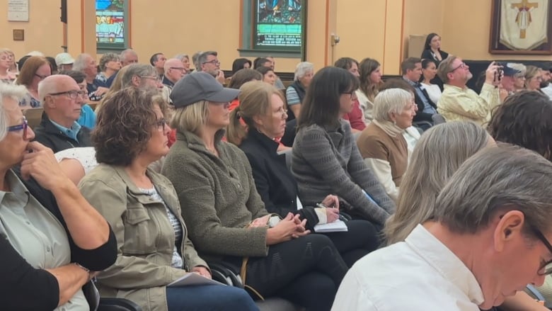 A crowd of people listen to the candidates answers. 