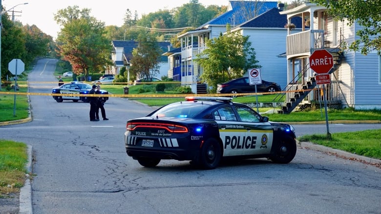 Police cars and yellow tape block off part of a residential road. 