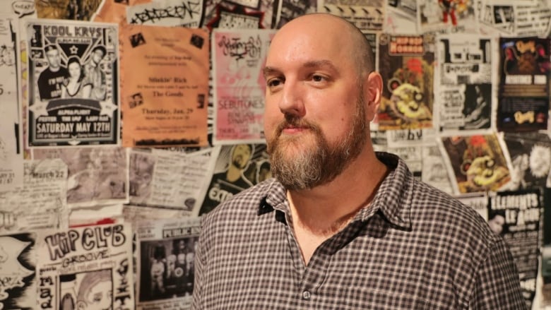 A man stands in front of a wall displaying hip-hope related posters