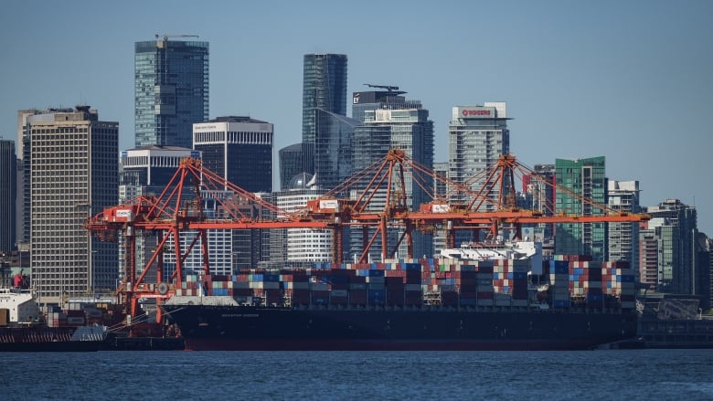  A container ship docked under gantry cranes at port and the downtown skyline are seen in Vancouver. 