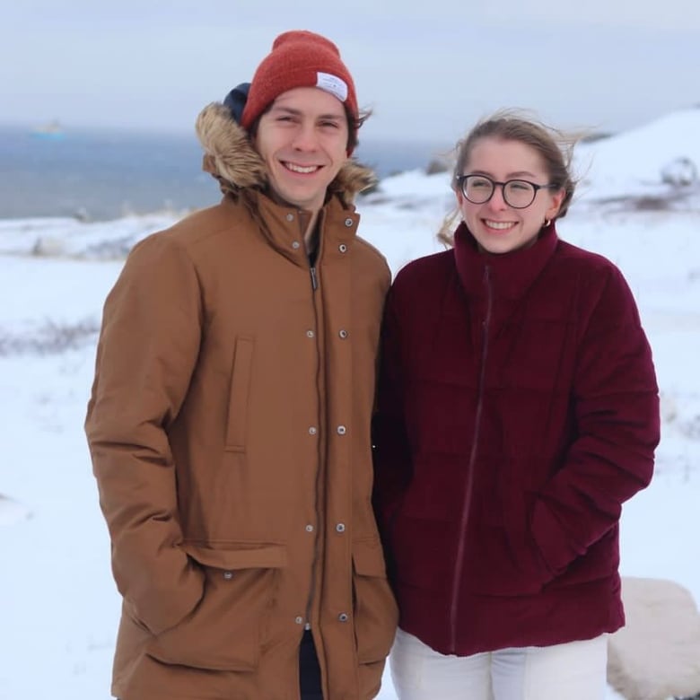 Man and woman in winter coats stand next to each other smiling in the snow.