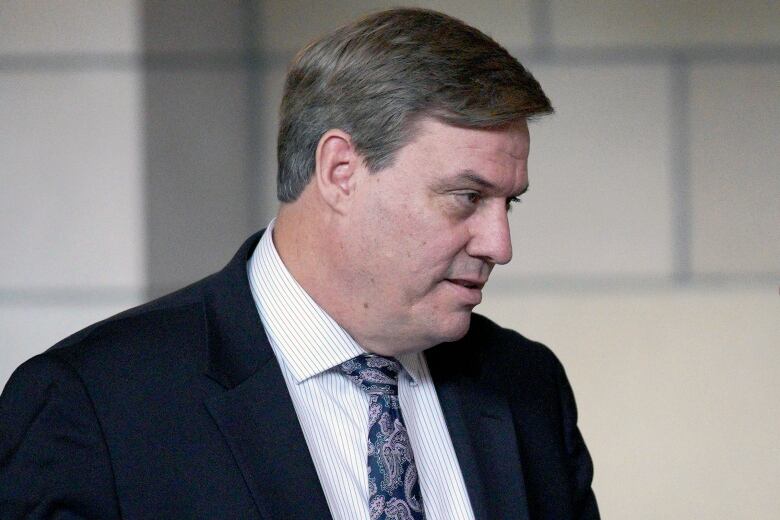 A cleanshaven man in a suit and tie is shown in a closeup photo.