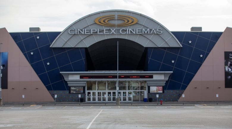 The front of a movie theatre is seen, in an empty parking lot. 