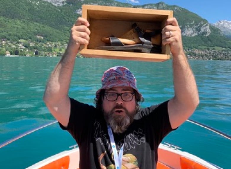 A man holds up a box containing a sandal in a boat. 